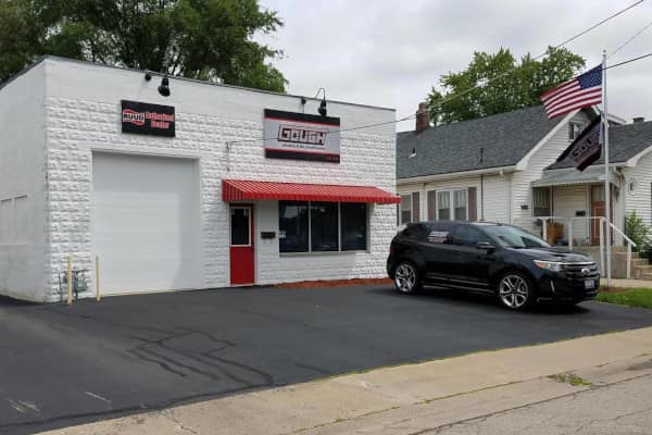 A building with signage indicating it is an HVAC business, featuring a white brick exterior, a red awning over the entrance, a large garage door, and a black SUV parked outside.