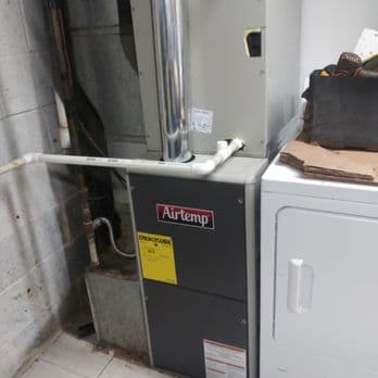 A gray Airtemp furnace unit is installed next to a washing machine in a utility area, with visible pipes and wiring around it.